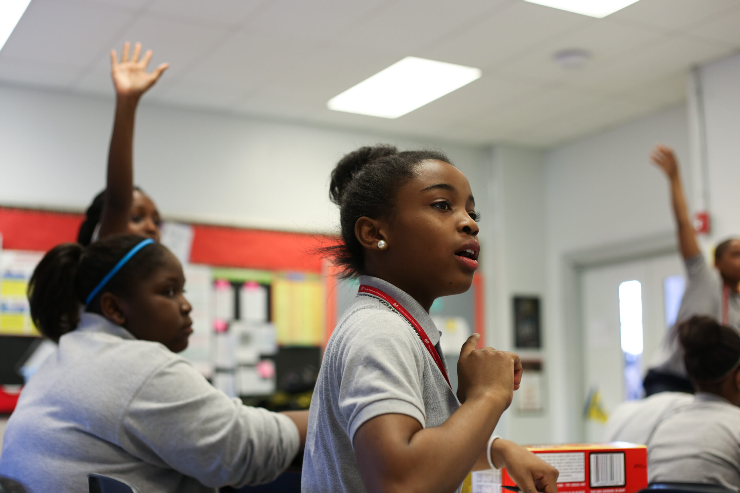 Classroom students engaged in an activity and raising their hands to volunteer